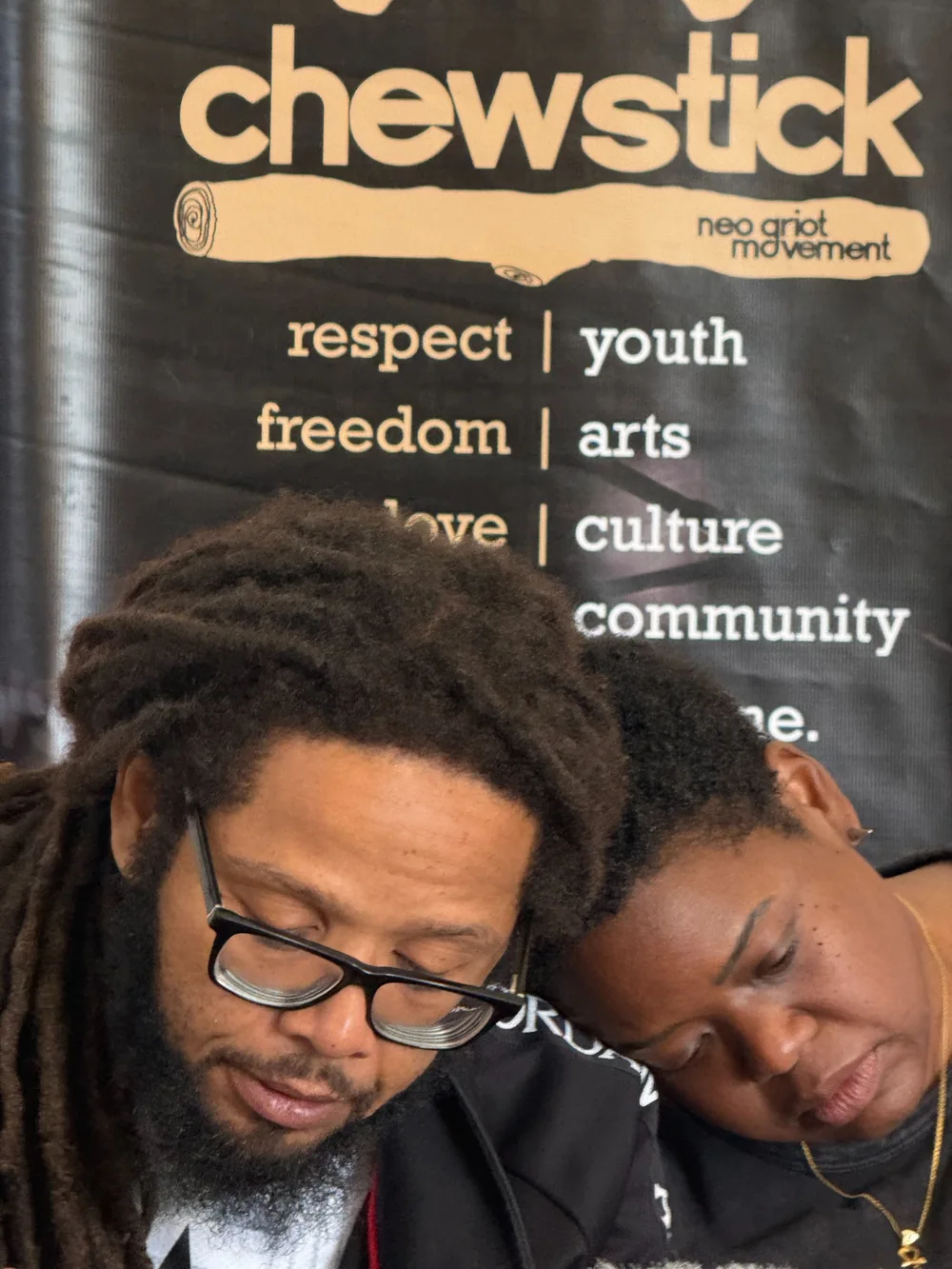 Two participants leaning together beneath a Chewstick banner