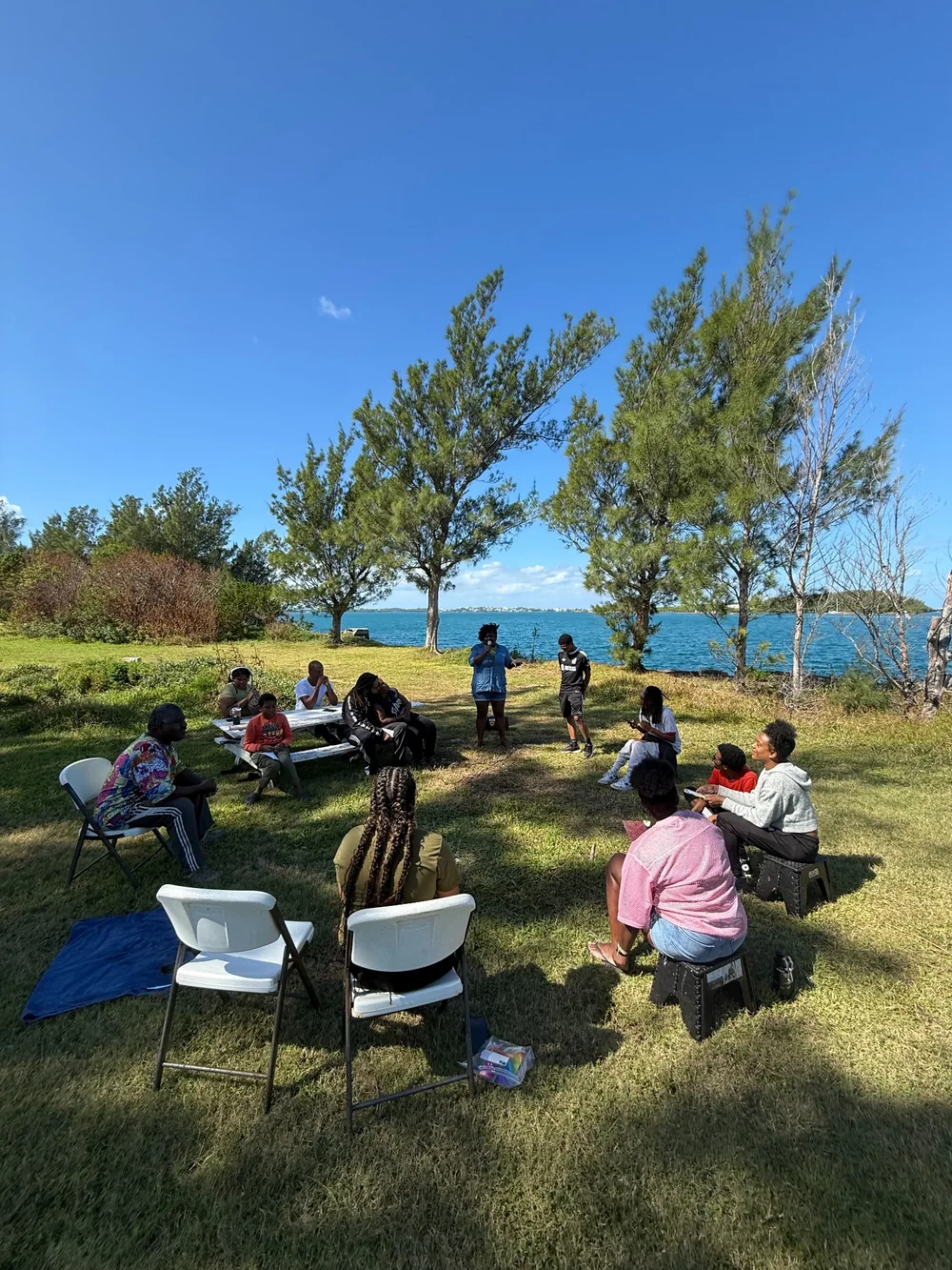 A group sitting in a circle outdoors beside the sea